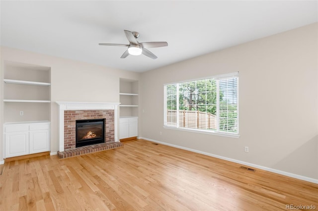 unfurnished living room with baseboards, built in shelves, ceiling fan, a fireplace, and light wood-type flooring