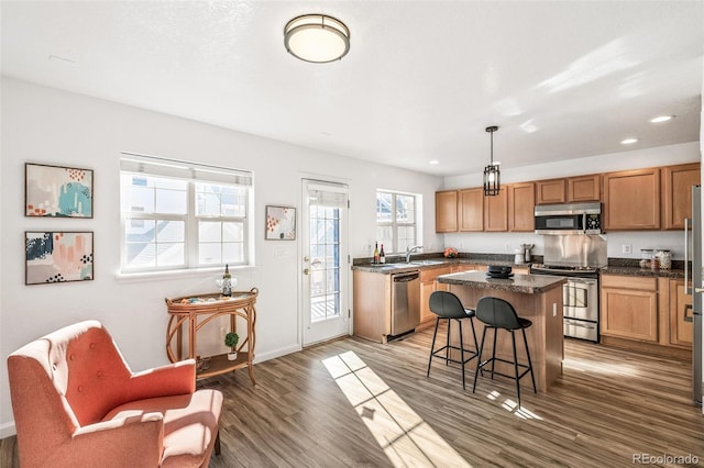 kitchen with pendant lighting, sink, dark wood-type flooring, stainless steel appliances, and a kitchen island