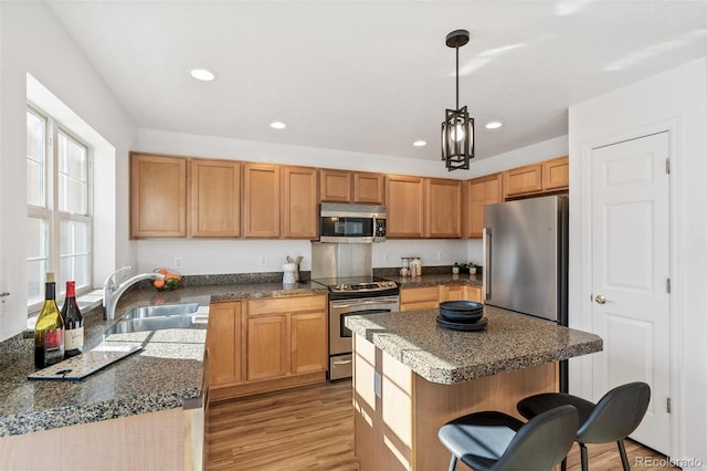 kitchen with a kitchen island, appliances with stainless steel finishes, sink, hanging light fixtures, and light hardwood / wood-style floors