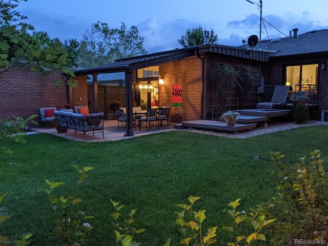 rear view of property featuring brick siding, an outdoor living space, a lawn, and a patio