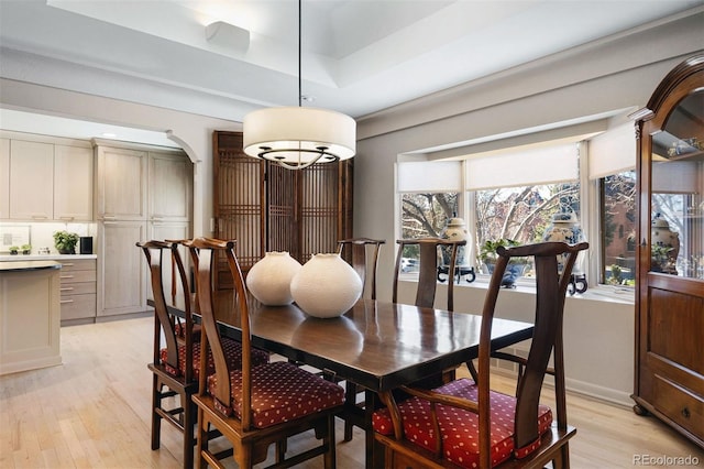 dining space with light wood-type flooring, arched walkways, and a raised ceiling