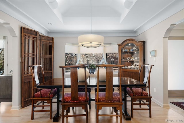 dining space with light wood finished floors, arched walkways, and a tray ceiling