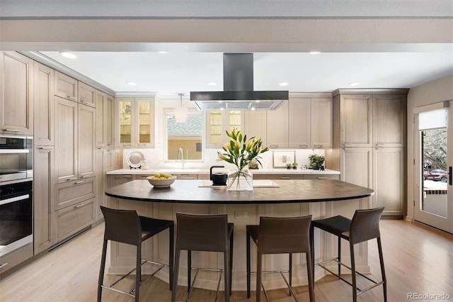 kitchen featuring light wood-style floors, a breakfast bar, and island exhaust hood