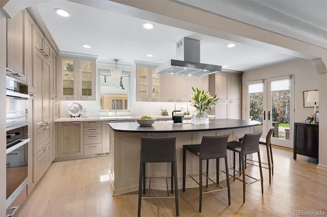 kitchen with a breakfast bar area, glass insert cabinets, light wood-style flooring, and range hood