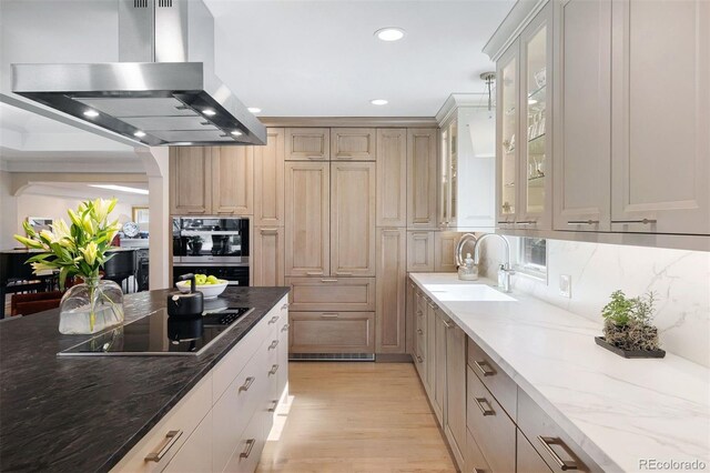 kitchen with island range hood, dark stone countertops, black electric cooktop, light wood-type flooring, and a sink