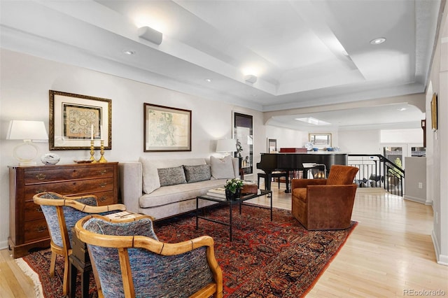 living area featuring light wood-style flooring, a tray ceiling, and baseboards