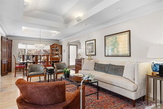 living area featuring light wood-style flooring, arched walkways, and a tray ceiling