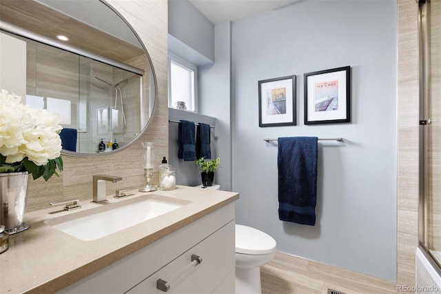 bathroom featuring vanity, a tile shower, toilet, and decorative backsplash