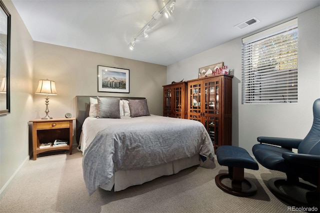 bedroom featuring baseboards, track lighting, visible vents, and light colored carpet