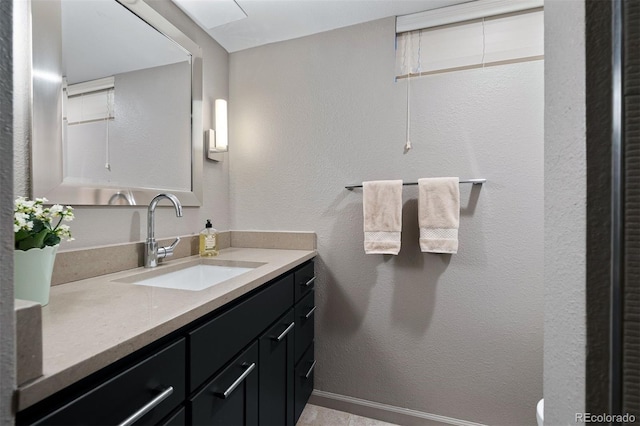 bathroom with a textured wall, vanity, and baseboards