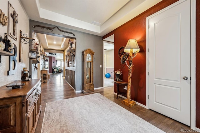 entrance foyer with a tray ceiling, visible vents, wood finished floors, and baseboards