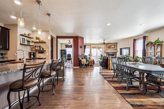 dining space with a ceiling fan, a fireplace, a textured ceiling, dark wood-style flooring, and recessed lighting