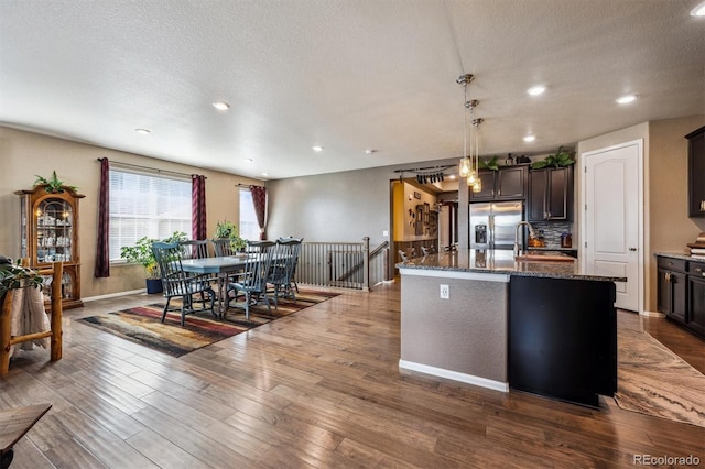 kitchen with recessed lighting, stainless steel fridge, dark stone countertops, and a sink