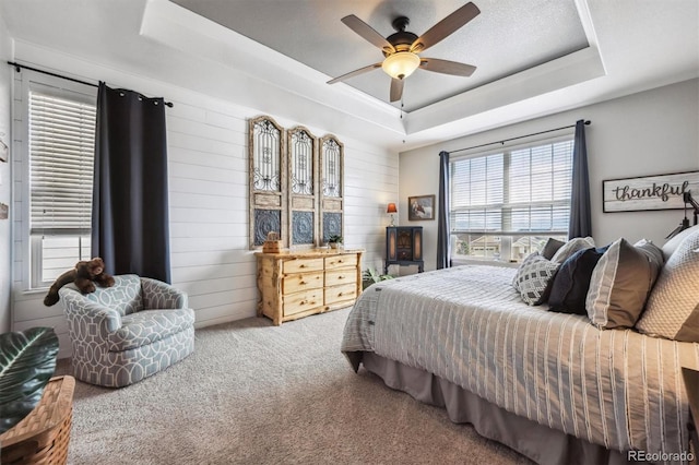 carpeted bedroom featuring wood walls, a tray ceiling, and ceiling fan