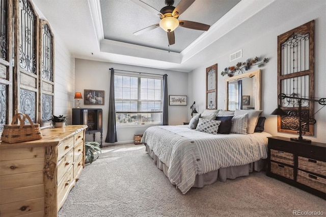 bedroom with a tray ceiling, carpet, ornamental molding, ceiling fan, and visible vents