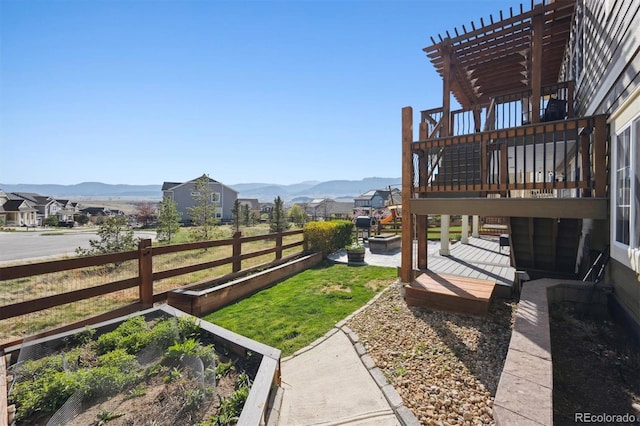 view of yard featuring a deck with mountain view, a pergola, a vegetable garden, and fence