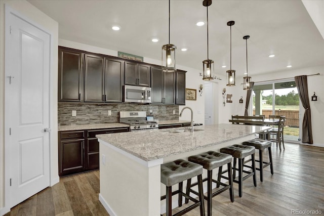 kitchen with a center island with sink, appliances with stainless steel finishes, a breakfast bar, pendant lighting, and sink