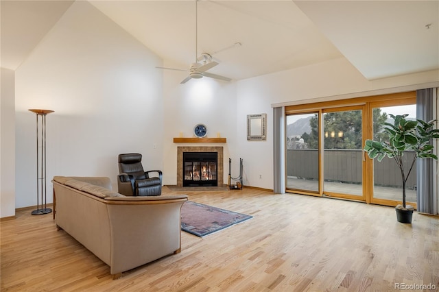 living room featuring lofted ceiling, a tile fireplace, ceiling fan, and light wood-type flooring