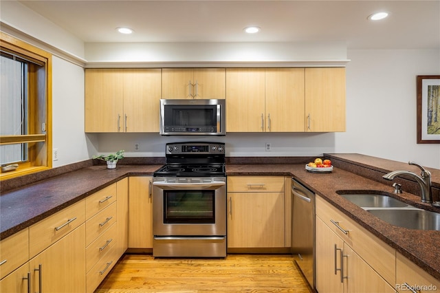 kitchen featuring light brown cabinetry, sink, dark stone counters, stainless steel appliances, and light hardwood / wood-style flooring