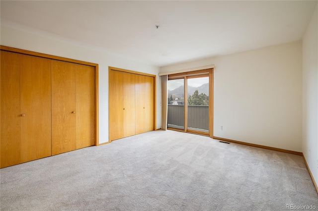 unfurnished bedroom featuring access to exterior, two closets, and light colored carpet