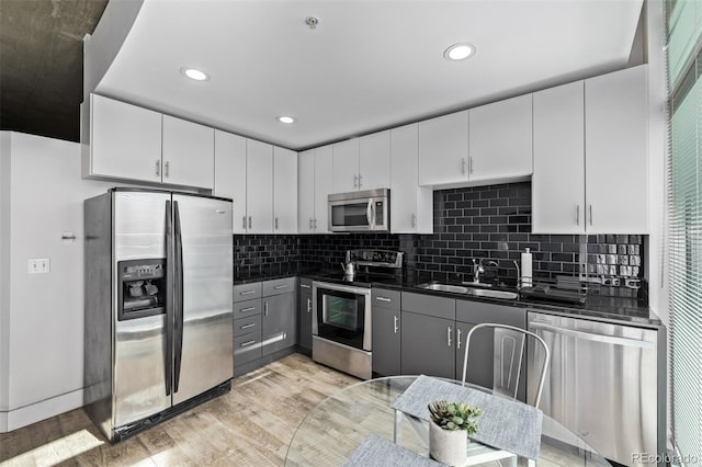 1700 Bassett St Unit 820, Denver, CO 80202 - kitchen featuring appliances with stainless steel finishes, a sink, dark countertops, light wood-style flooring, and white cabinetry