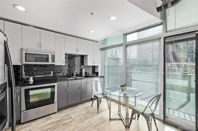 1700 Bassett St Unit 820, Denver, CO 80202 - kitchen featuring appliances with stainless steel finishes, dark countertops, backsplash, light wood-type flooring, and white cabinets