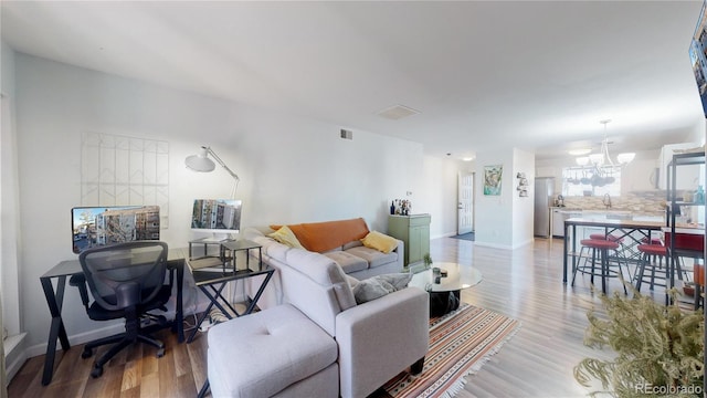 living room with sink, light wood-type flooring, and an inviting chandelier