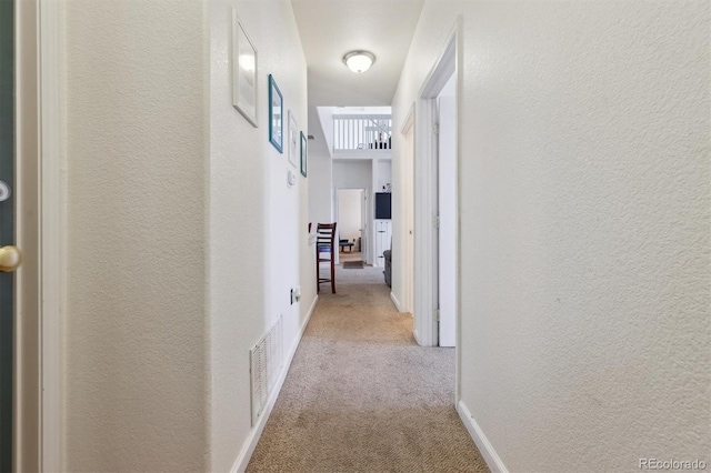 hall featuring carpet, visible vents, a textured wall, and baseboards