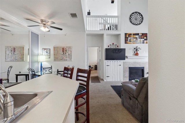 carpeted dining space featuring a sink, visible vents, a ceiling fan, a tiled fireplace, and crown molding