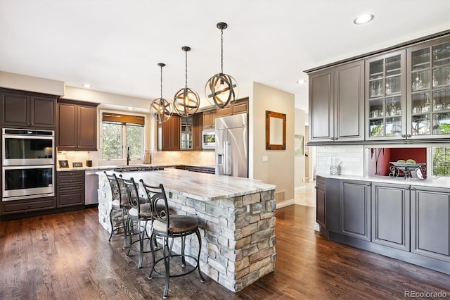 9065 E Lost Hill Trl, Lone Tree, CO 80124 - kitchen with built in appliances, dark wood-style floors, tasteful backsplash, glass insert cabinets, and a breakfast bar