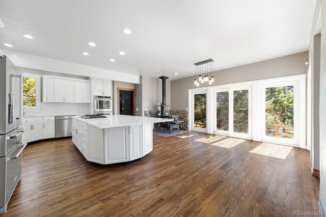 kitchen with appliances with stainless steel finishes, a kitchen island, white cabinets, hanging light fixtures, and dark hardwood / wood-style floors