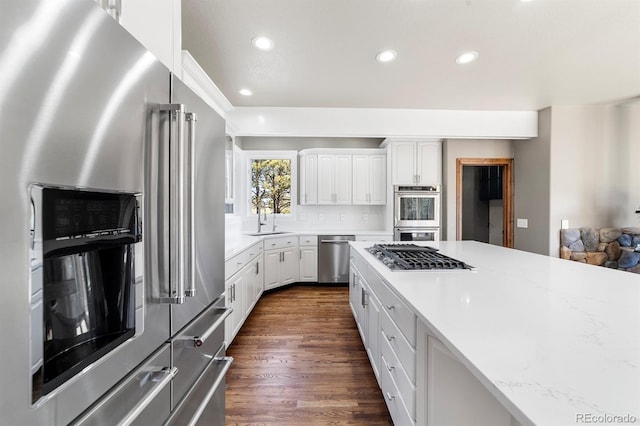 kitchen with white cabinets, dark wood-type flooring, stainless steel appliances, light stone counters, and tasteful backsplash