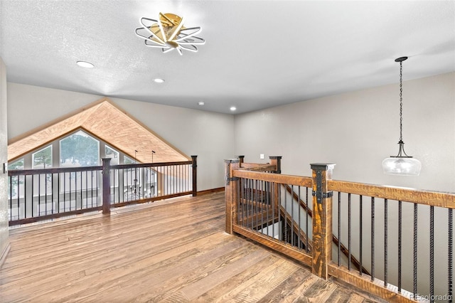 hallway featuring hardwood / wood-style flooring, vaulted ceiling, and a textured ceiling