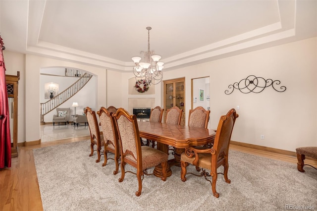 22554 Treetop Ln, Golden, CO 80401 - dining space with a tray ceiling, a chandelier, a glass covered fireplace, baseboards, and arched walkways