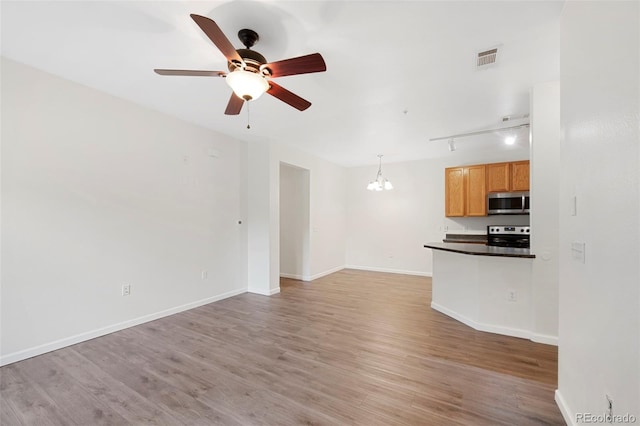 unfurnished living room with visible vents, track lighting, baseboards, ceiling fan with notable chandelier, and light wood-style floors