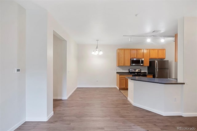 kitchen featuring stainless steel appliances, dark countertops, light wood-style flooring, and a notable chandelier