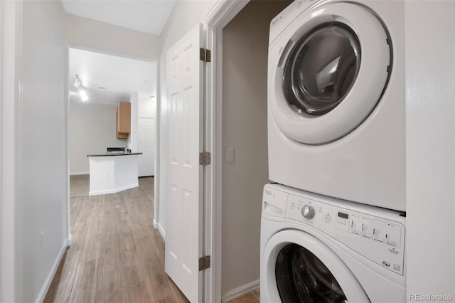 laundry room featuring baseboards, stacked washer and dryer, light wood-style flooring, and laundry area