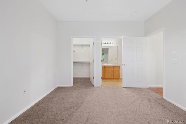 unfurnished bedroom featuring baseboards, a sink, a spacious closet, a closet, and light colored carpet