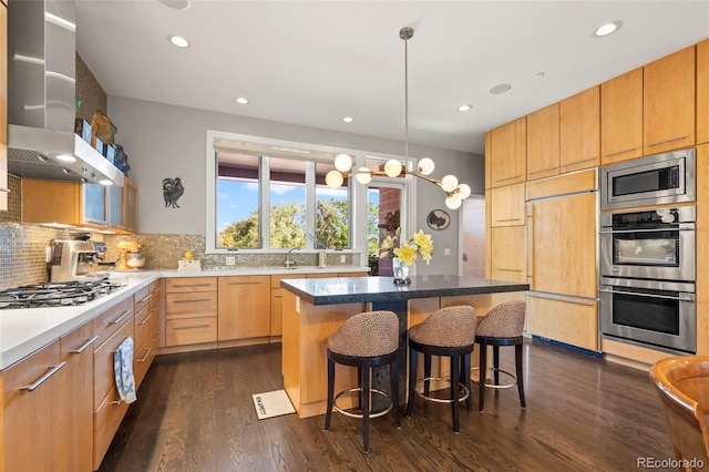 kitchen featuring built in appliances, dark wood-type flooring, a breakfast bar area, a kitchen island, and wall chimney exhaust hood