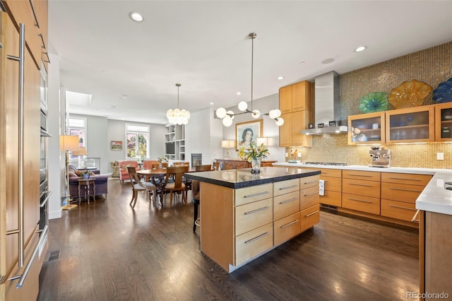 kitchen featuring a center island, dark hardwood / wood-style floors, hanging light fixtures, wall chimney range hood, and an inviting chandelier