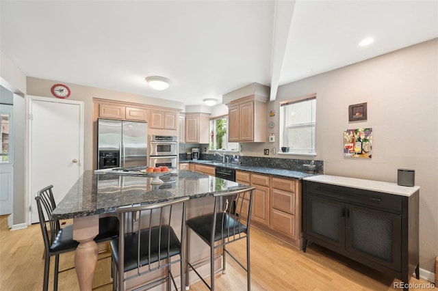 kitchen featuring appliances with stainless steel finishes, light hardwood / wood-style floors, dark stone counters, sink, and a kitchen island