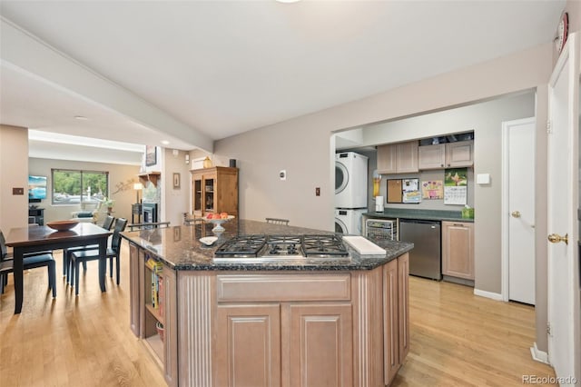 kitchen with light wood-type flooring, stainless steel appliances, a center island, dark stone counters, and stacked washer / drying machine