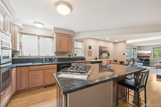 kitchen with light wood-type flooring, stainless steel appliances, a kitchen island, and dark stone countertops