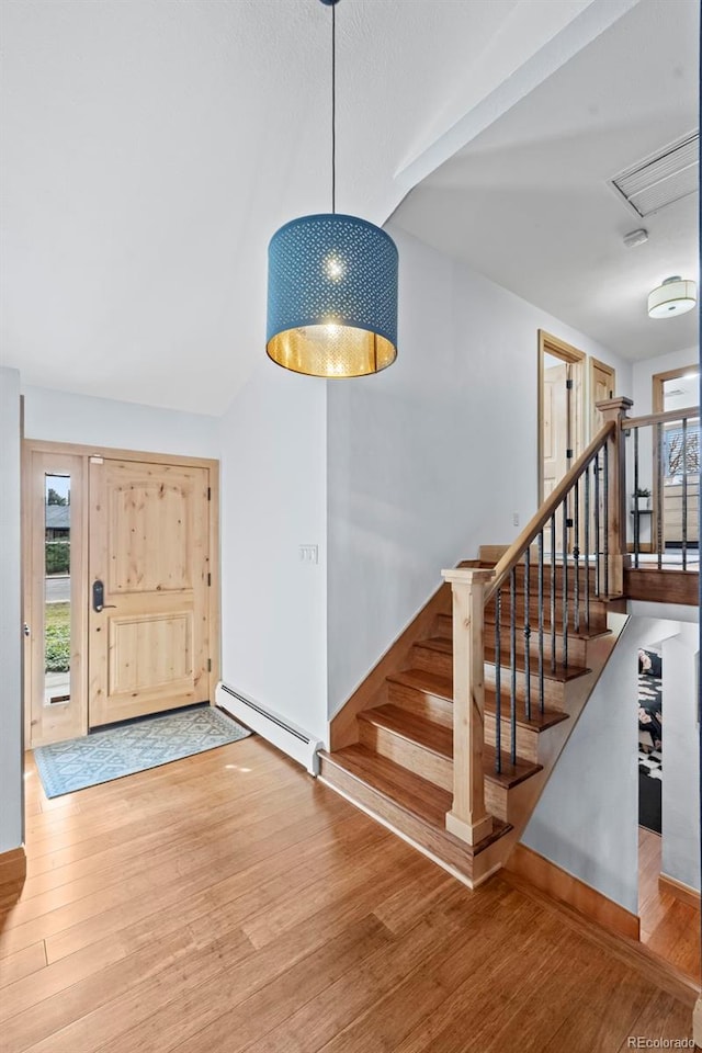 entrance foyer with baseboard heating, wood finished floors, and stairs