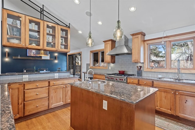 kitchen featuring stainless steel stove, dark stone counters, wall chimney exhaust hood, and a sink