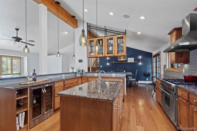 kitchen featuring an island with sink, a sink, high end stainless steel range oven, wall chimney exhaust hood, and lofted ceiling