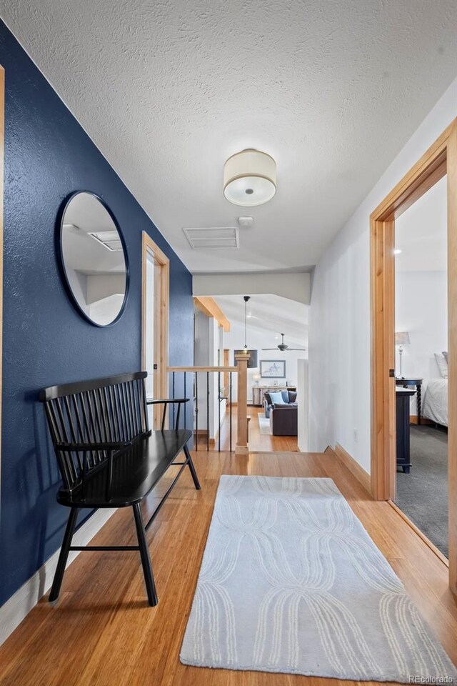 corridor with baseboards, attic access, an upstairs landing, wood finished floors, and a textured ceiling