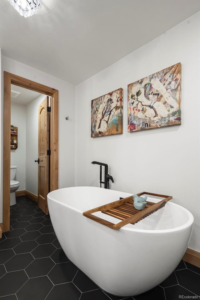 bathroom featuring tile patterned floors, a soaking tub, toilet, and baseboards