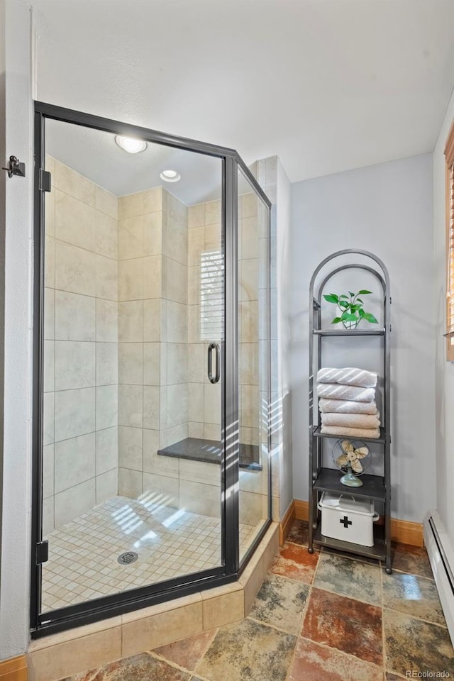 bathroom with baseboards, baseboard heating, stone tile flooring, and a shower stall