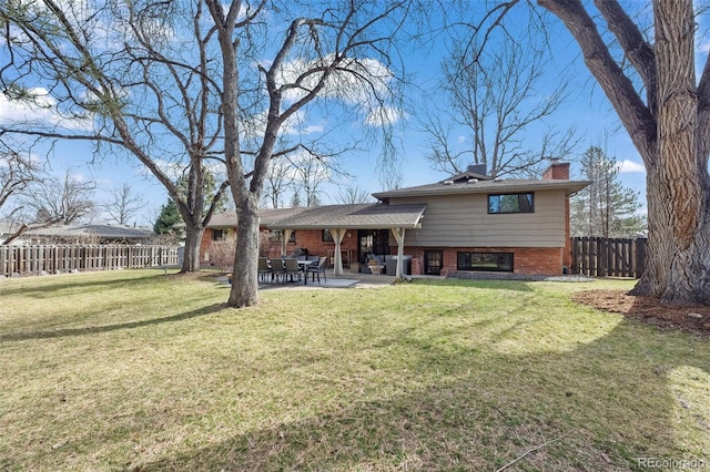 rear view of house with brick siding, fence private yard, a chimney, a yard, and a patio area